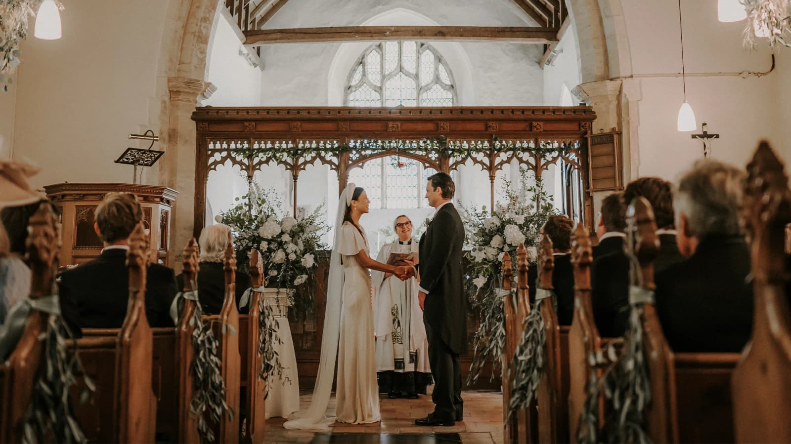 With white flowers either side, the couple say their vows before a smiling female vicar