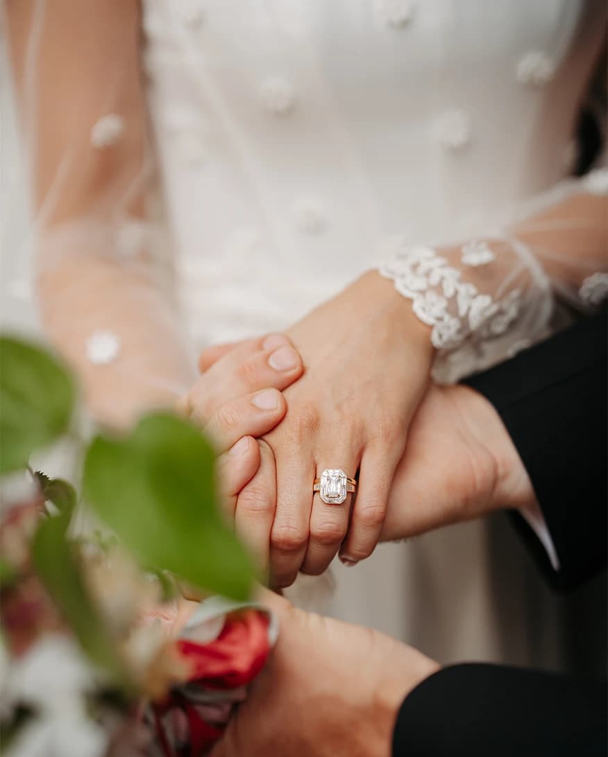 The bride's hand with her new ring, held by the groom against her lace-cuffed sleeve and embellished dress