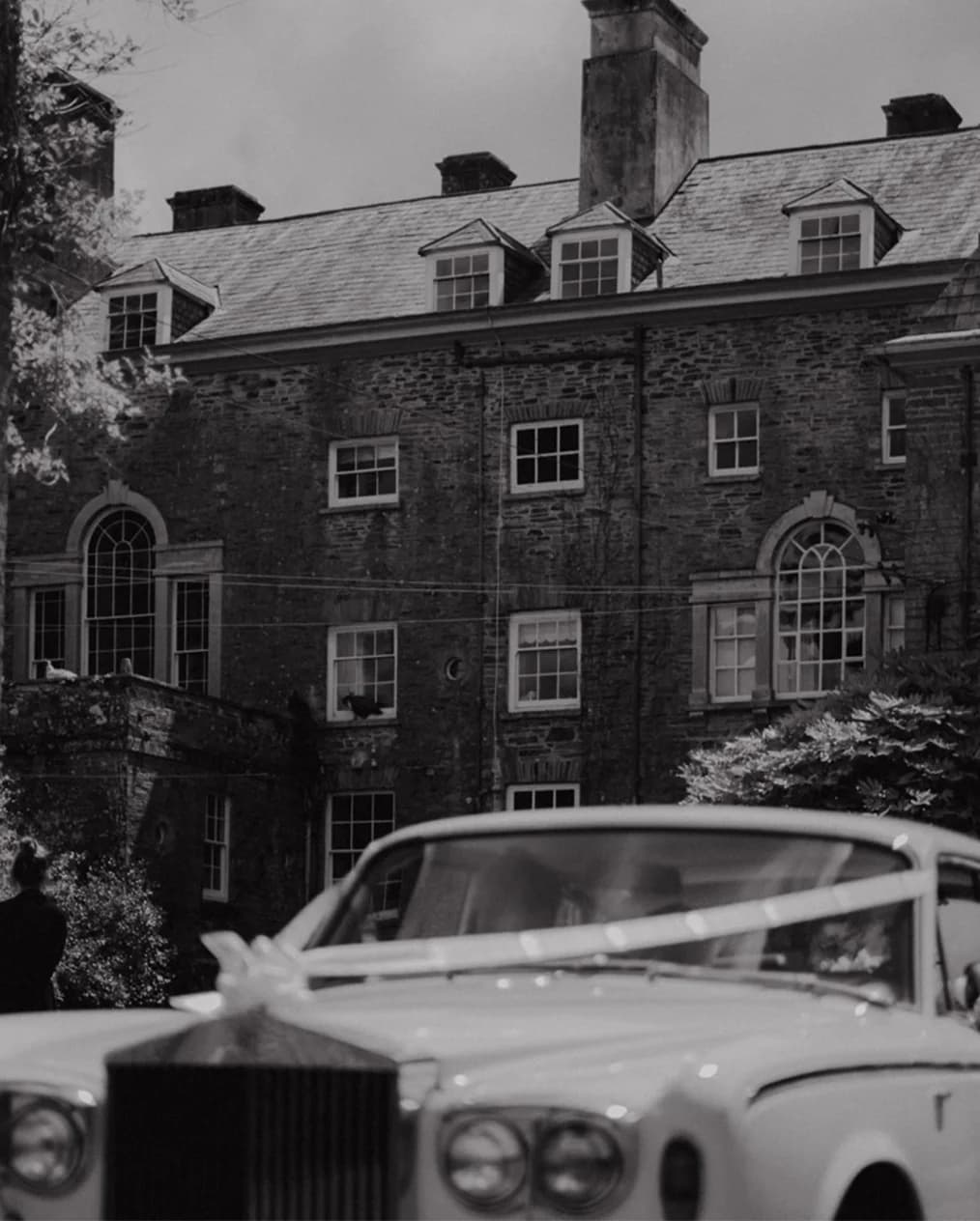 White rolls royce decorated with white ribbons parked in front of the wedding venue