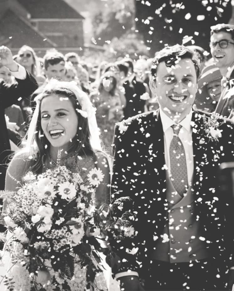 Bride and groom leave the church ceremony while confetti and thrown at them