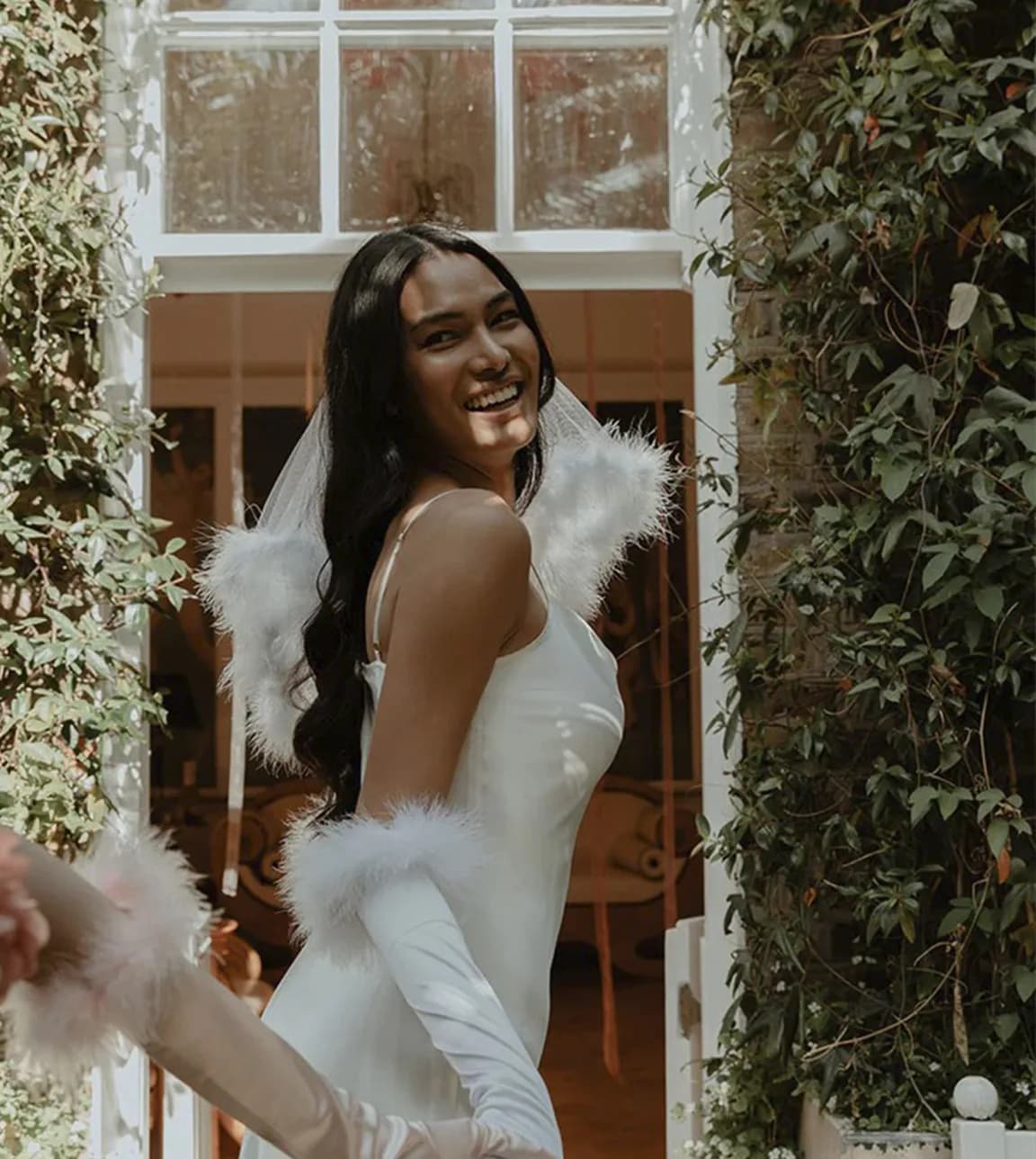 Future bride wears white satin gloves and veil with feathers and enjoys her hen do party outside.