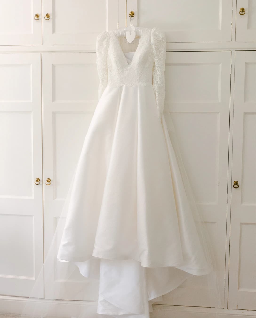 Prepared wedding dress hangs on wardrobe doors white shoes on floor 