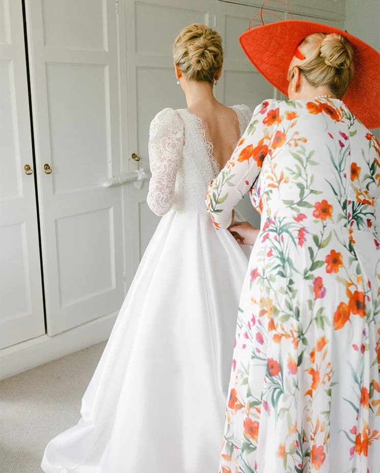 Mother of the bride helps bride with dressing ahead of her wedding ceremony.