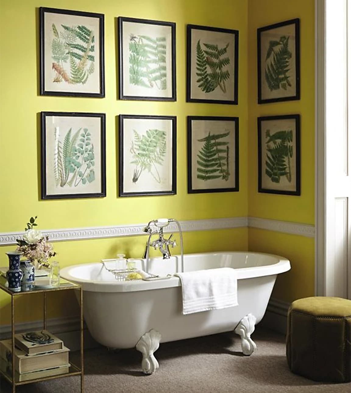 Gallery wall with black framed fern prints is placed above a traditional bath in yellow bathroom