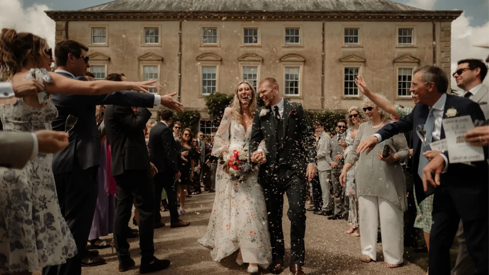 Bride and groom walking out from their wedding at a stone mansion in Cornwall with guests throwing confetti