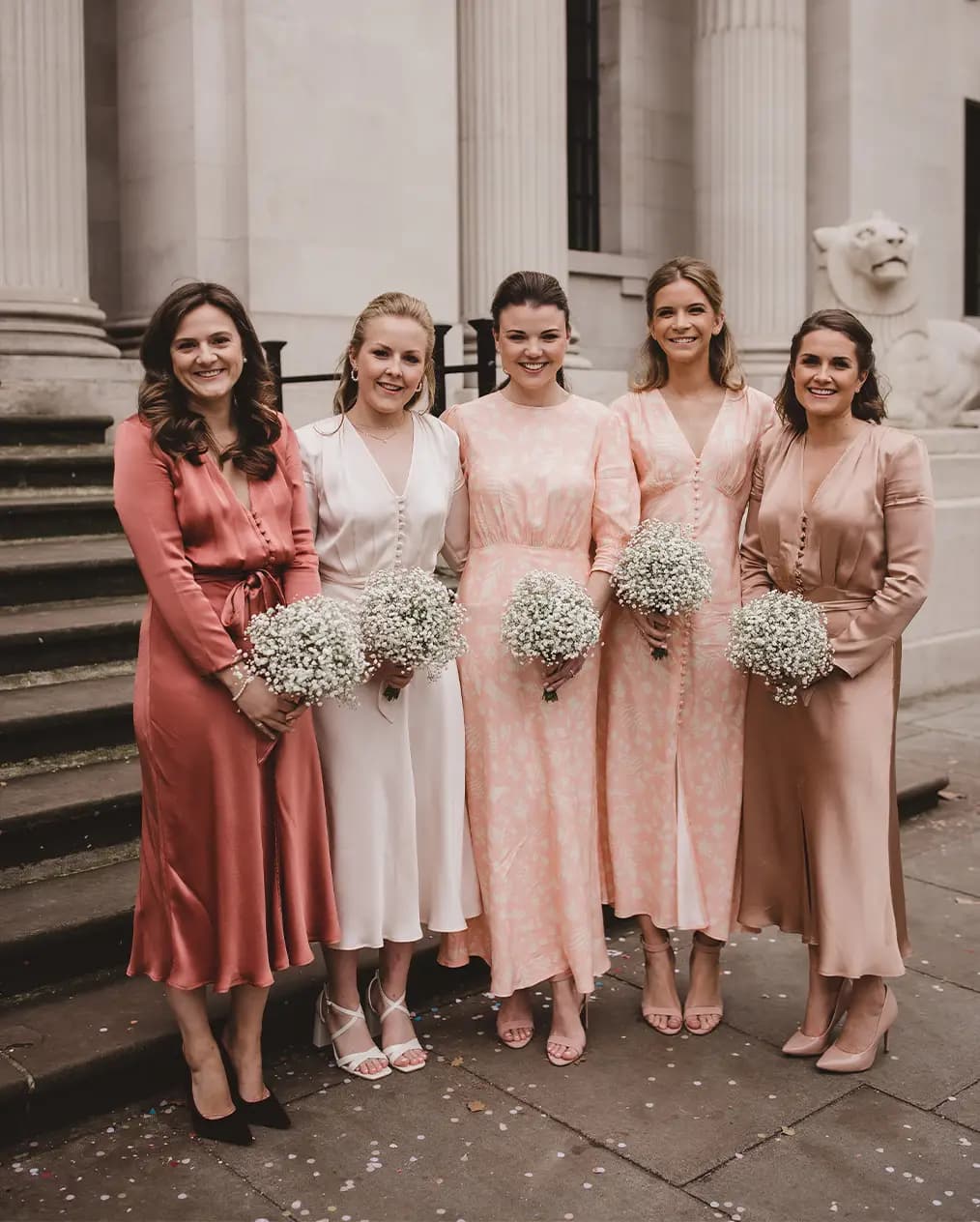 Bridesmaids wearing different pink dresses and holding white bouquets