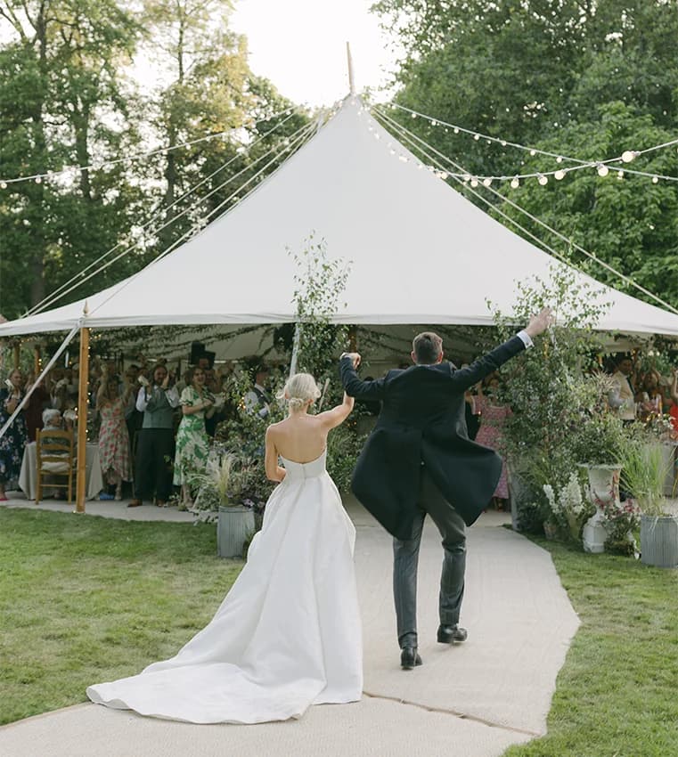 Happy bride and groom walk towards the trational wedding marquee of their English garden inspired wedding in Hampshire.