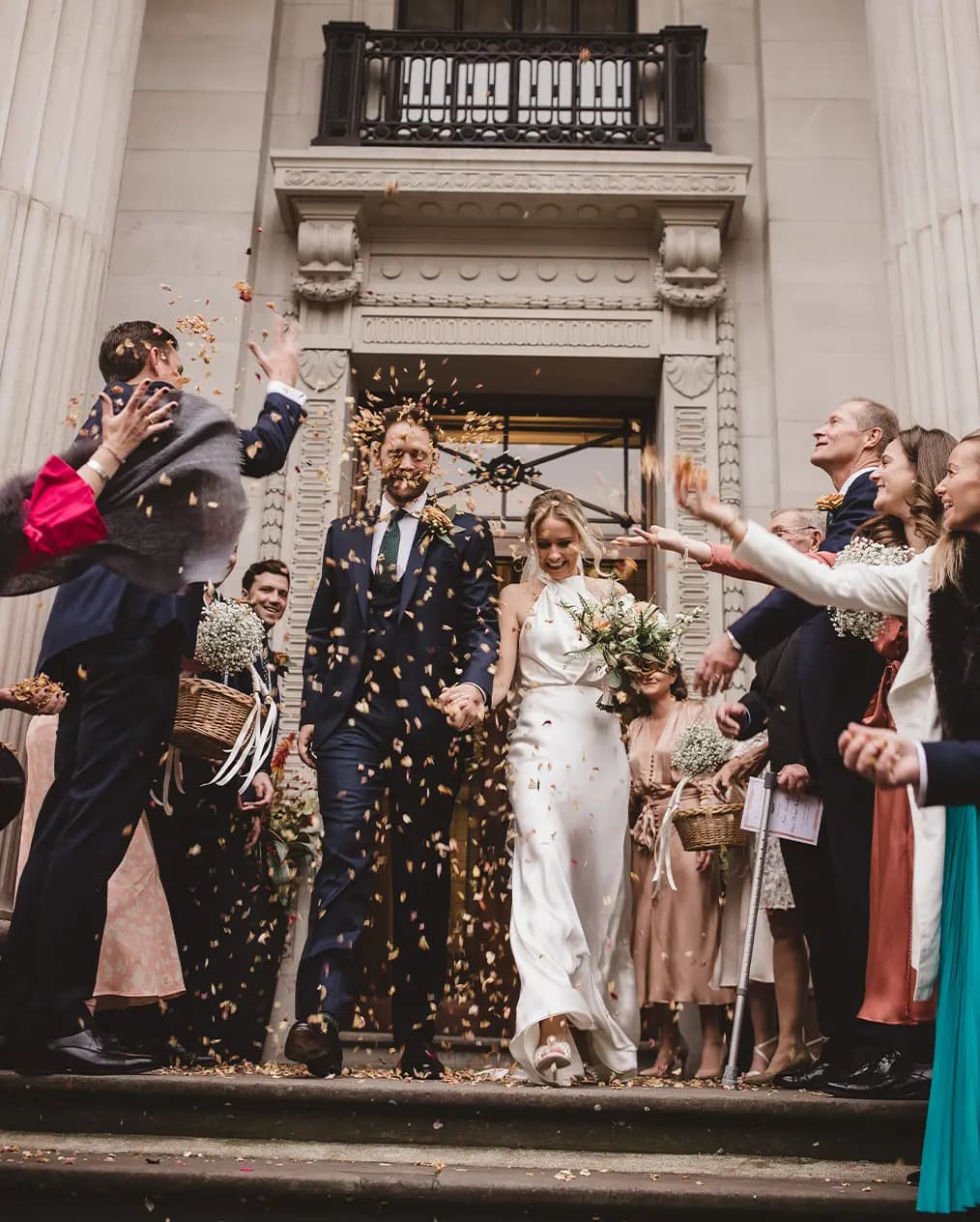 Bride and groom walking out of the wedding venue at Marylebone Town Hall with guests throwing dried flowers as confetti