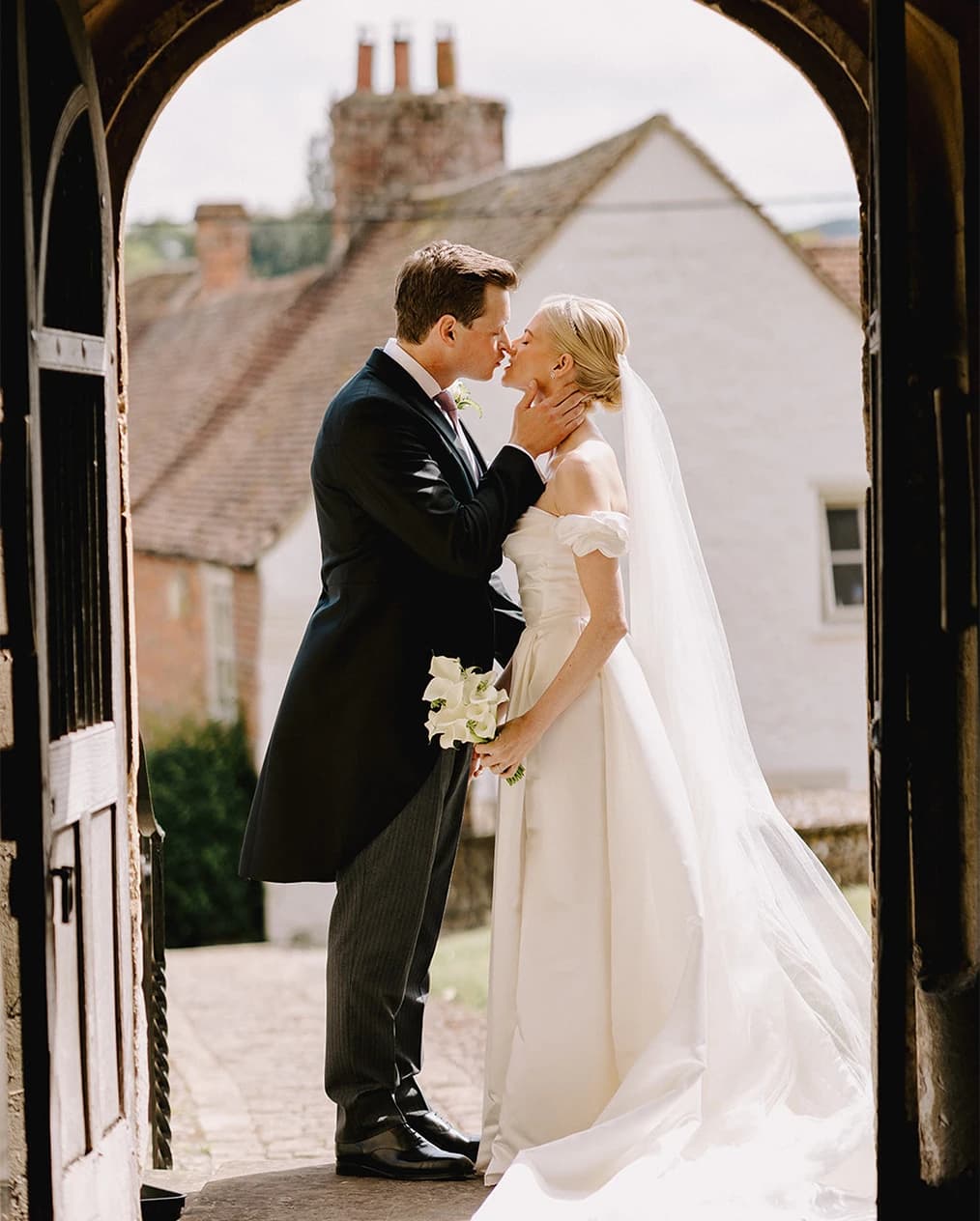 Bride with veil and groom in morning suit are kissing outside the traditional English church