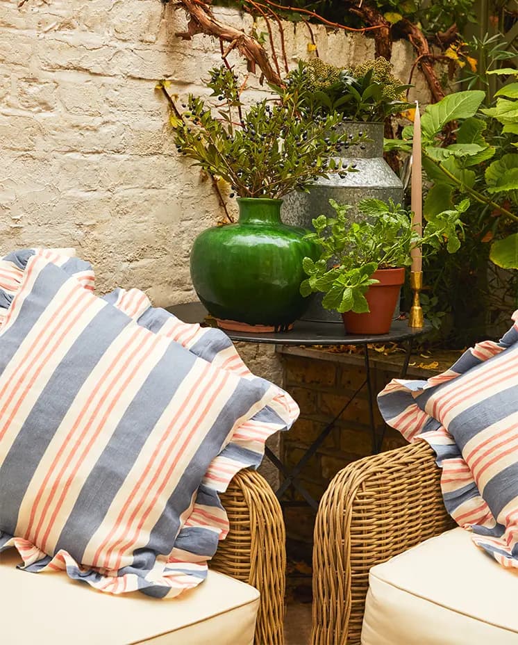 Rattan furniture with homeware wedding presents: striped Amuse La Bouche frilled cushions and green plants placed behind.