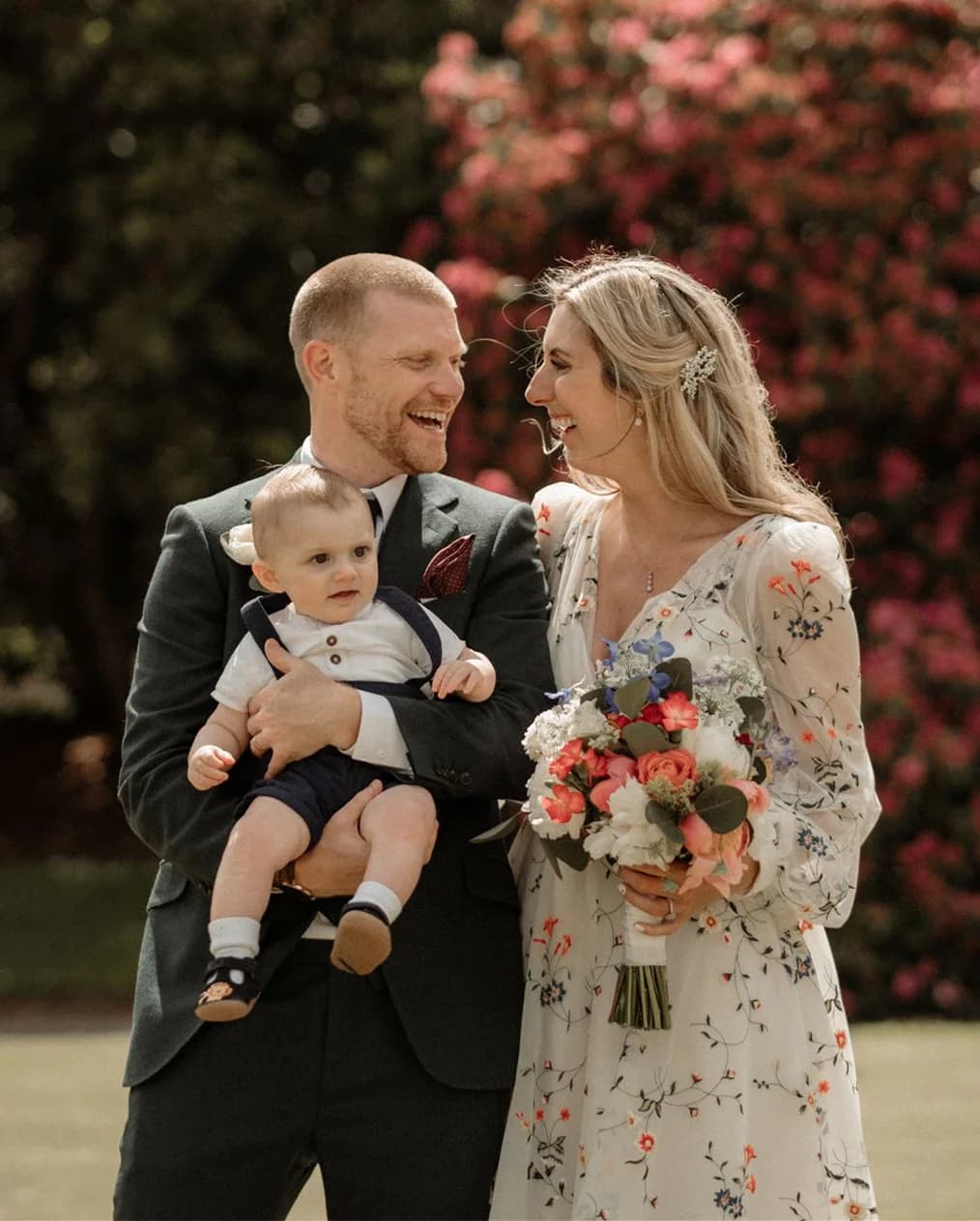 Bride and groom with their baby son while the bride holds her wedding bouquet of pink and white flowers