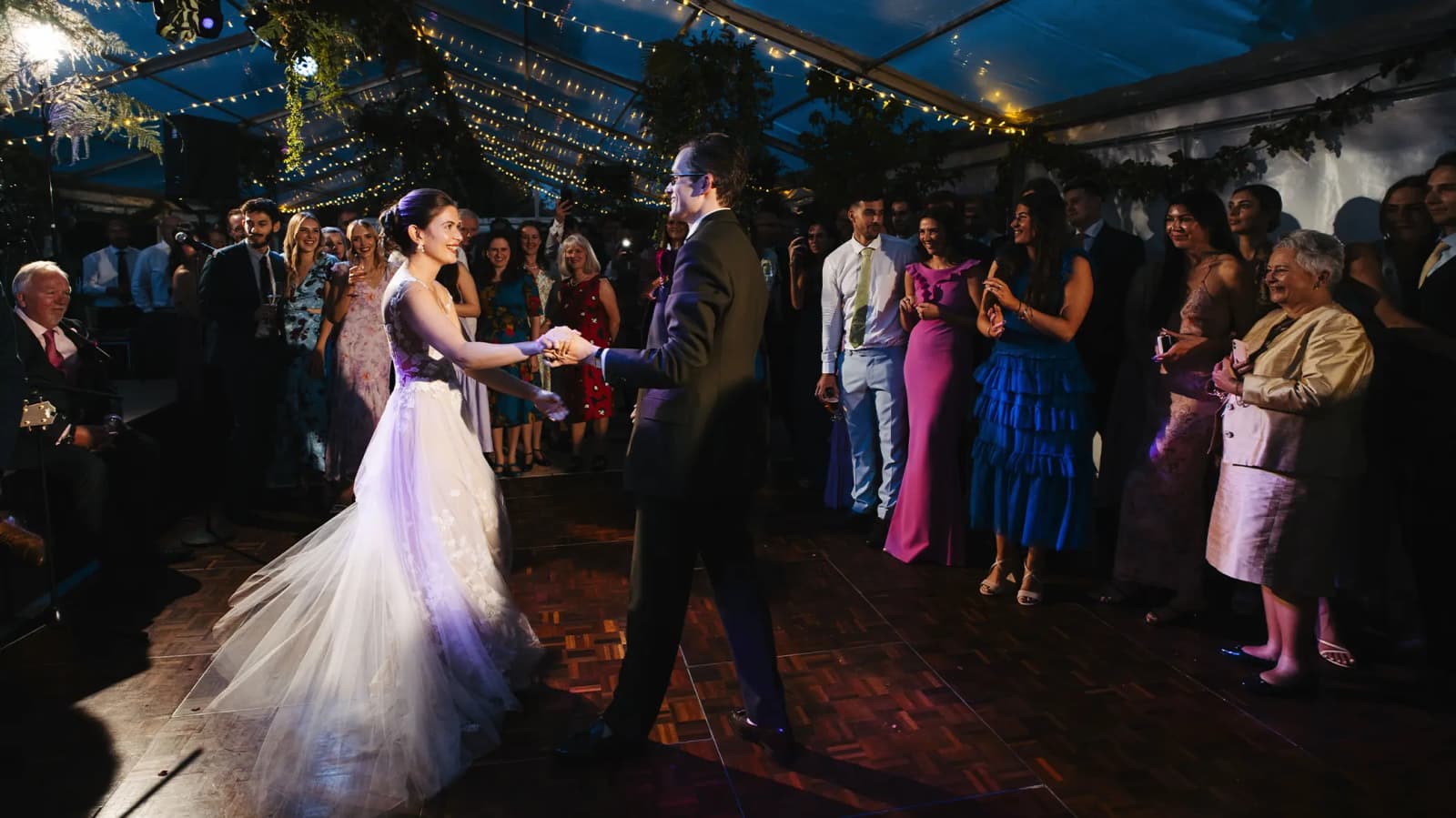 Bride and groom do a traditional first dance during their evening wedding party with festoon lights.