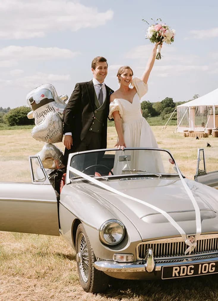 The Wedding Present Company bride and groom wave from the vintage car