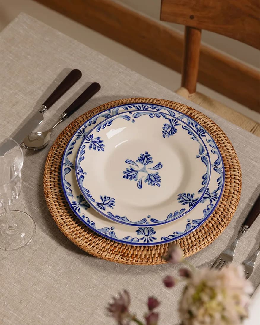 A table setting with Rebecca Udall blue plate on rattan placemat