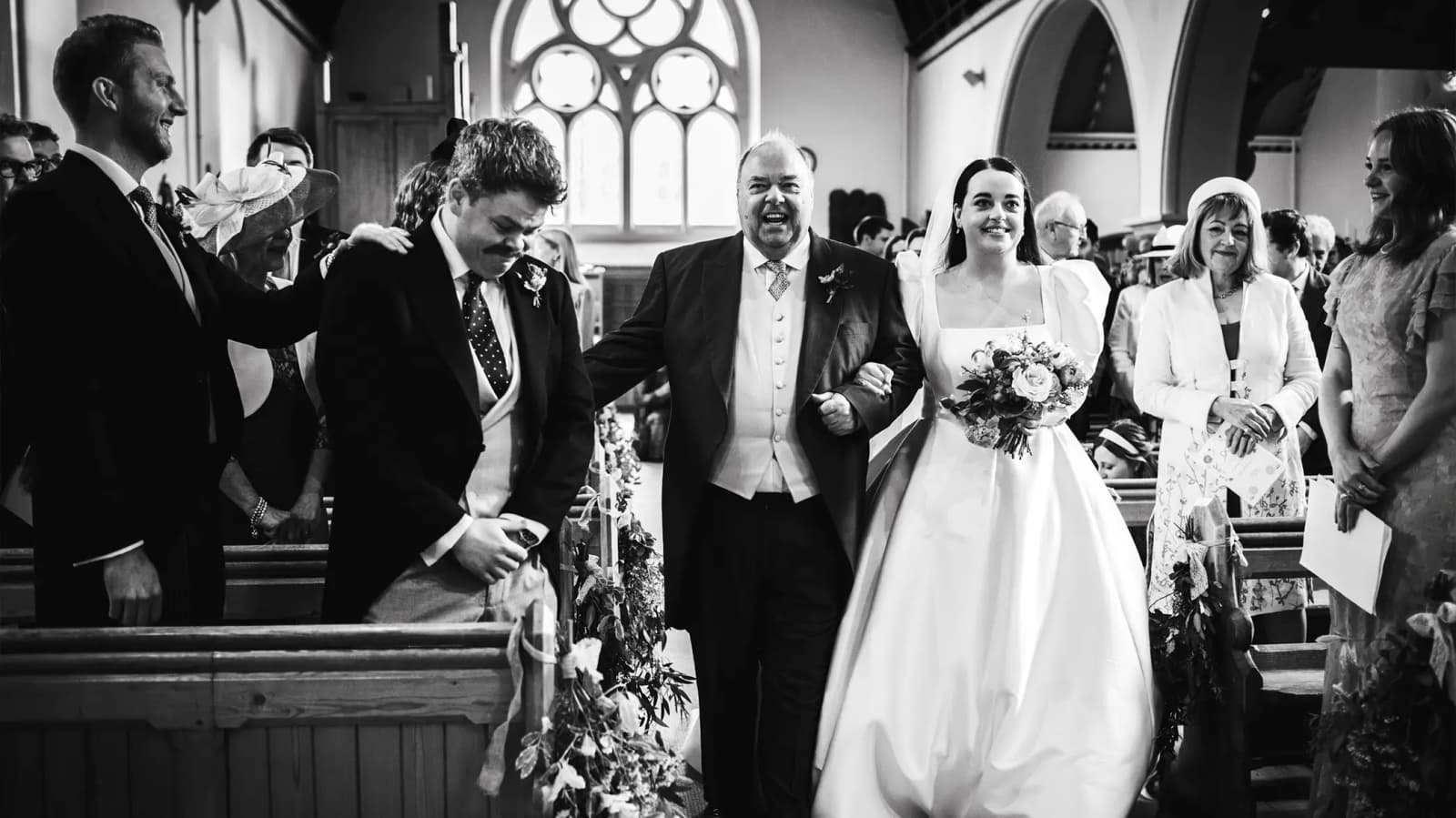 Groom is stand up in church while the bride walks down aisle with her father.