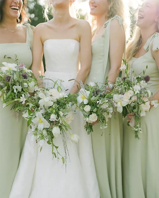 Bride and bridesmaids wearing sage green dresses wear delicate seasonal bouquets.
