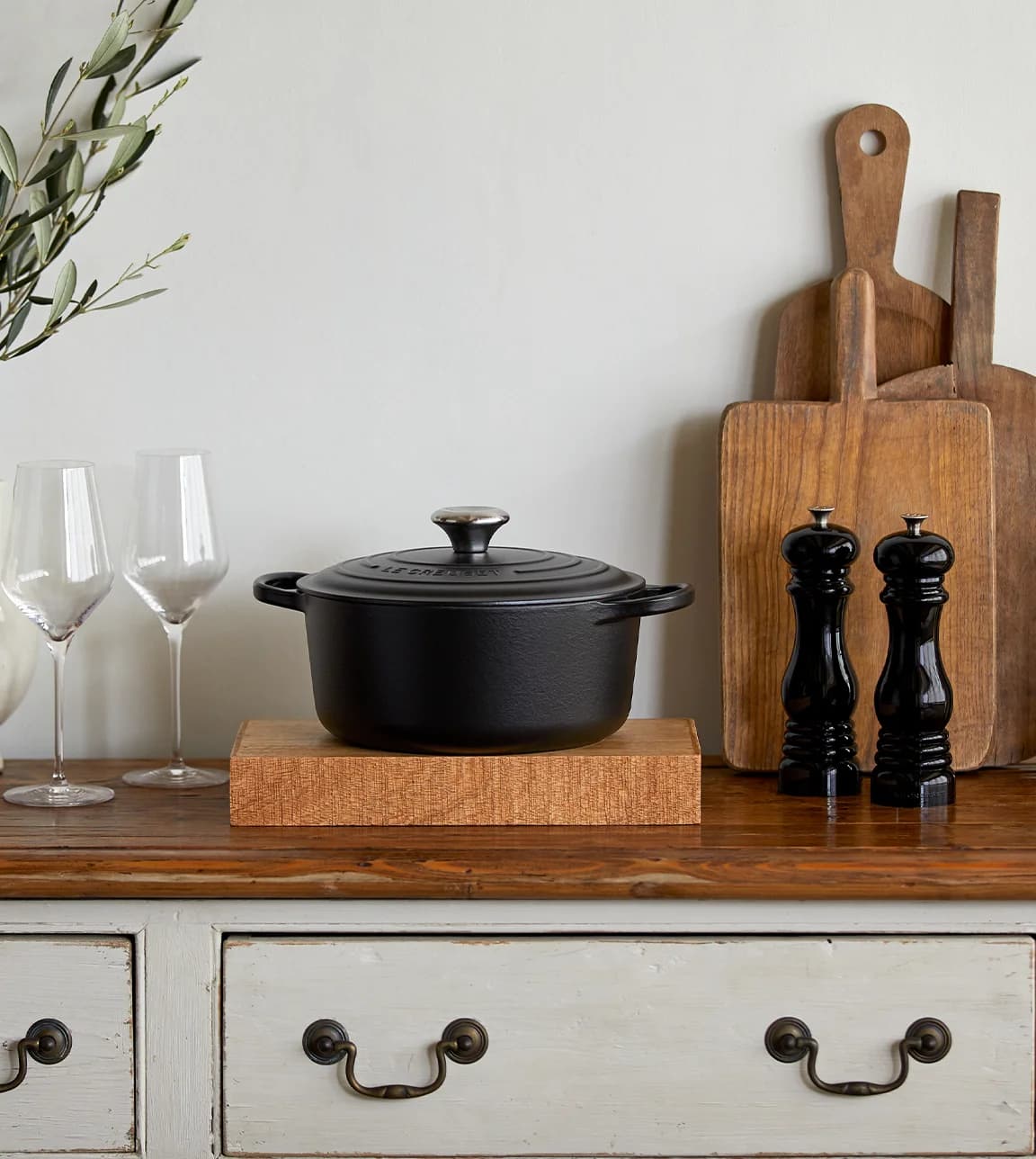 A traditional kitchen counter with Le Creuset round casserole in Satin black placed next to the wooden cutting boards 