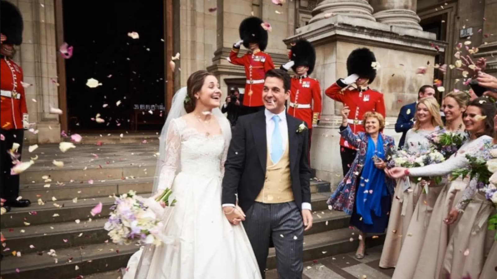 Husband and wife walking out of the church with guests throwing confetti and soldiers in the background