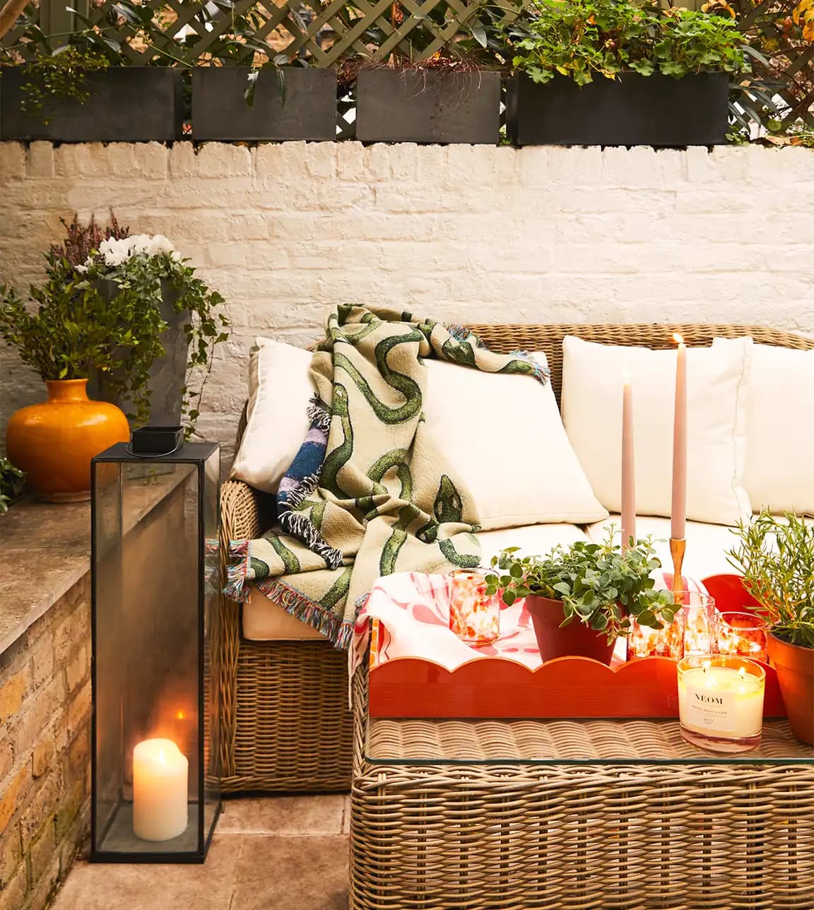 A cosy London terrace with rattan furniture and black lanterns, featuring Rosalyn's homeware wedding gifts: throw, scalloped drink tray and brass candleholders
