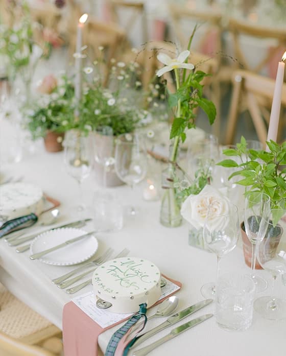 Delicate wedding table decor surrounded by simple green and wild flower foliage in light colours