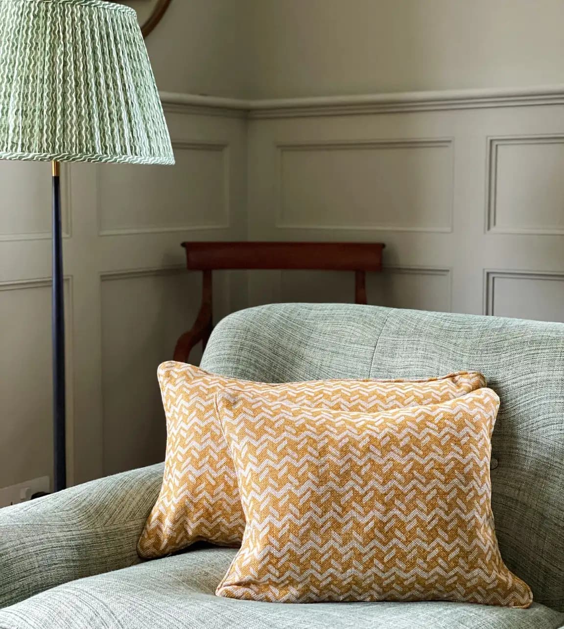 Green Feromoie lampshade and  mustard yellow cushions are styled on a sofa in the living room.