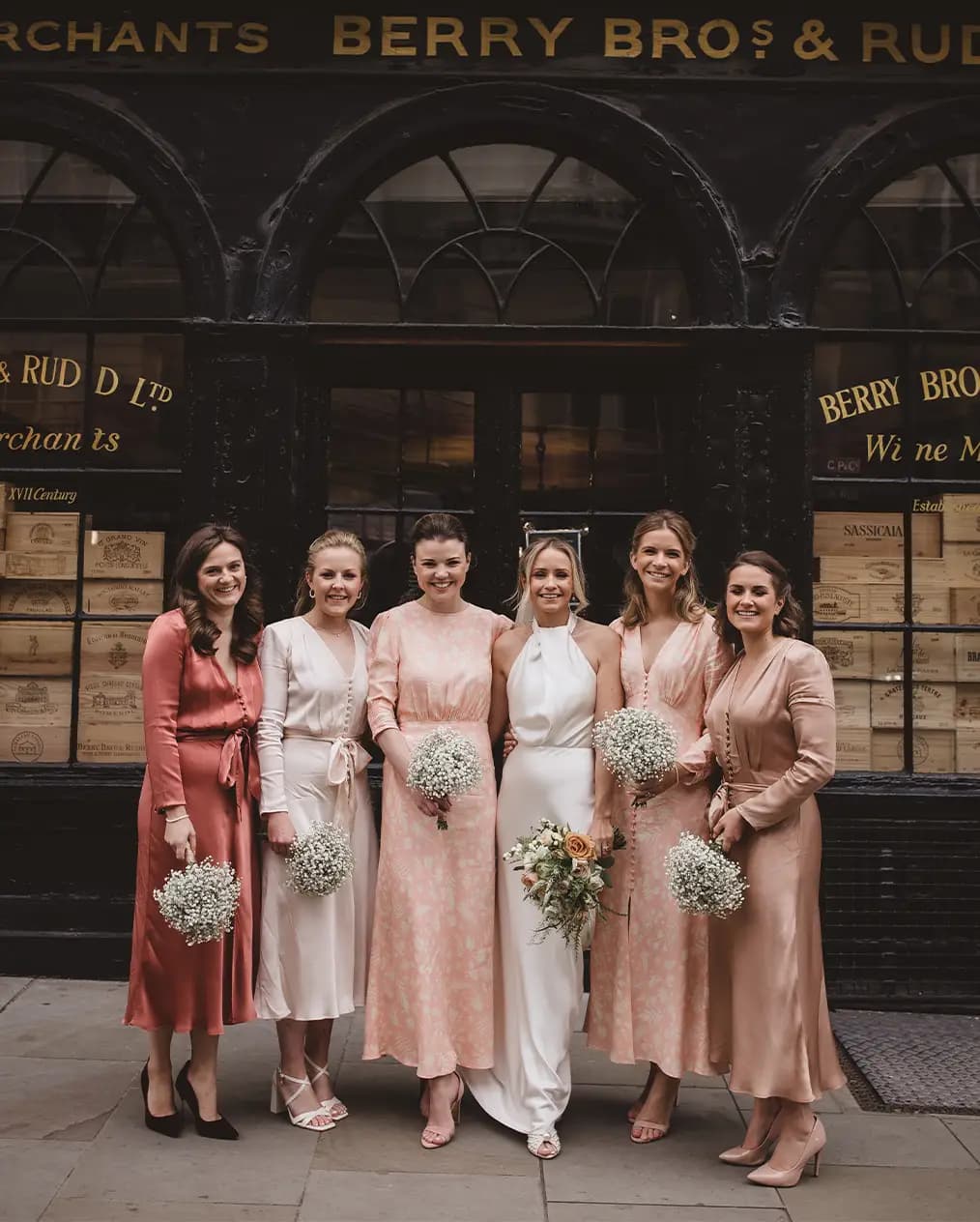 Bridal party standing in front of London reception venue with bridesmaids wearing mismatching pink dresses