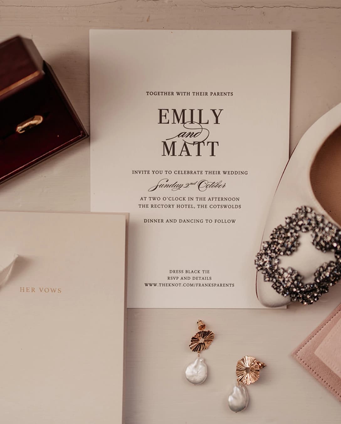 A timeless wedding invite and bride's vows placed next to wedding bands, bride's jewellery and shoes.