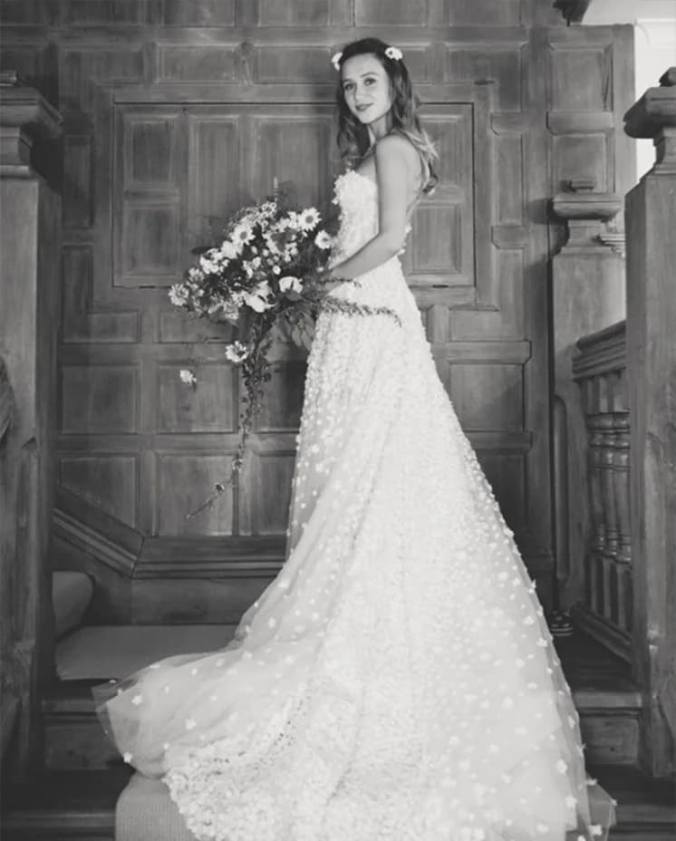 Bride stands on stairs wearing strapless dress with flower applique