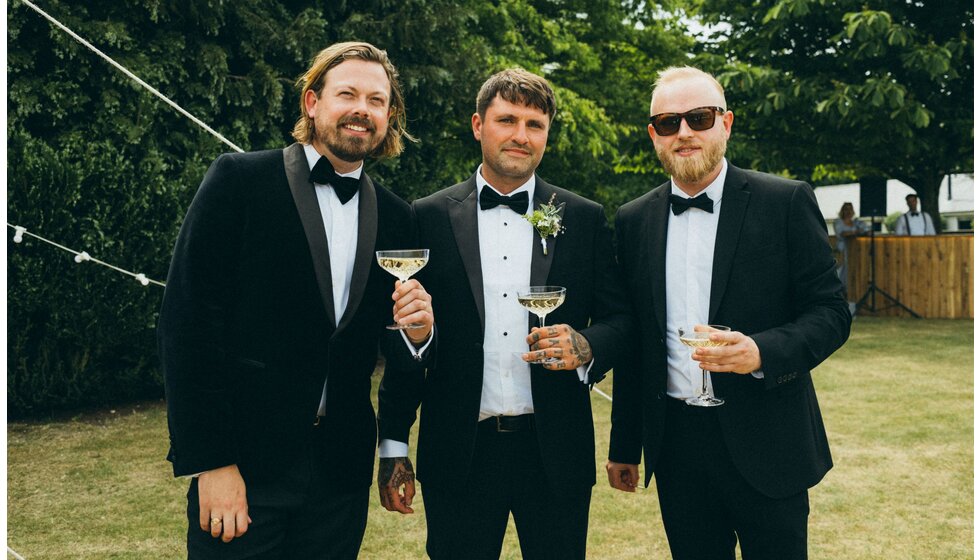 Whimsical Tuscan-Inspired Wedding in Hampshire | Groom's party in black suits holding champagne coupes