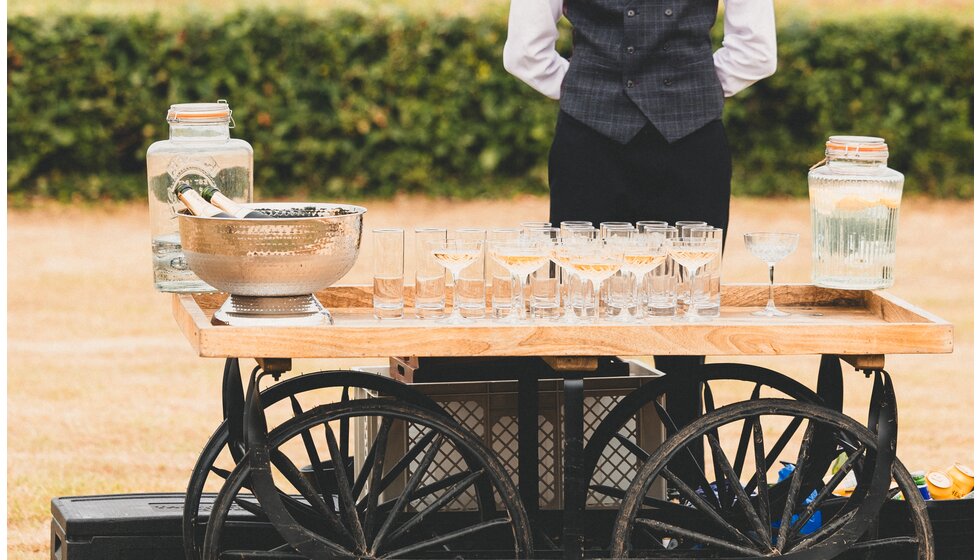 Whimsical Tuscan-Inspired Wedding in Hampshire | A bartender standing next to a vintage wedding bar cart with champagne