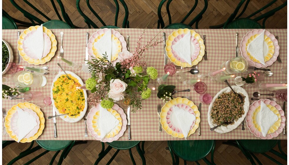 Supper Club with Skye McAlpine | A bird's eye view of a table with a gingham tablecloth, beautifully set with pink and yellow tableware, platters with food