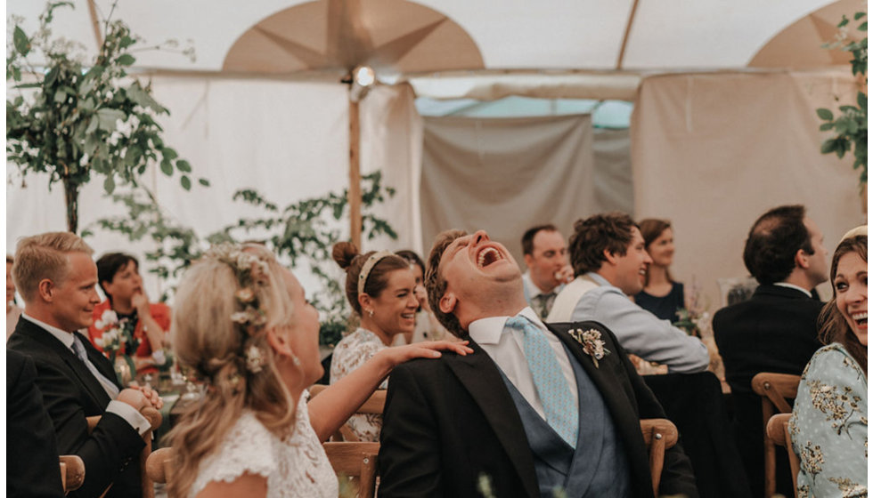 The image captures the groom laughing during the speeches.