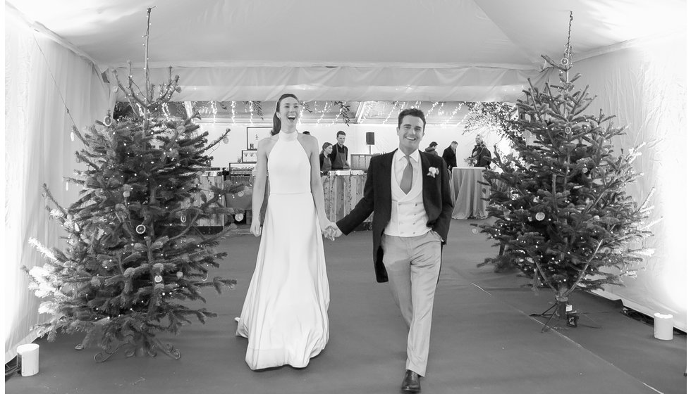 The bride and groom walk into their marquee past the Christmas trees.