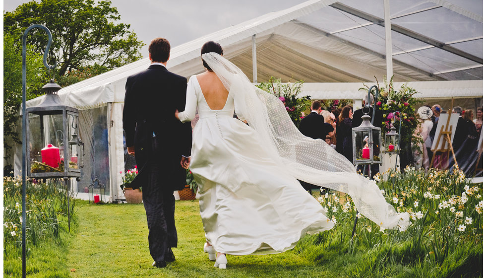 The bride and groom walking into their marquee. 