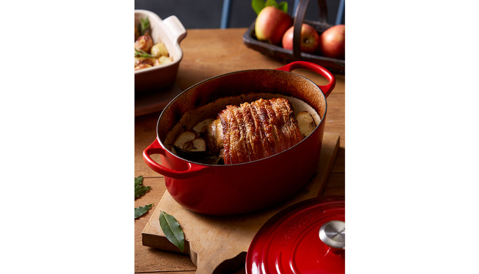 A red oval cast iron casserole dish from Le Creuset with cooked pork belly inside.