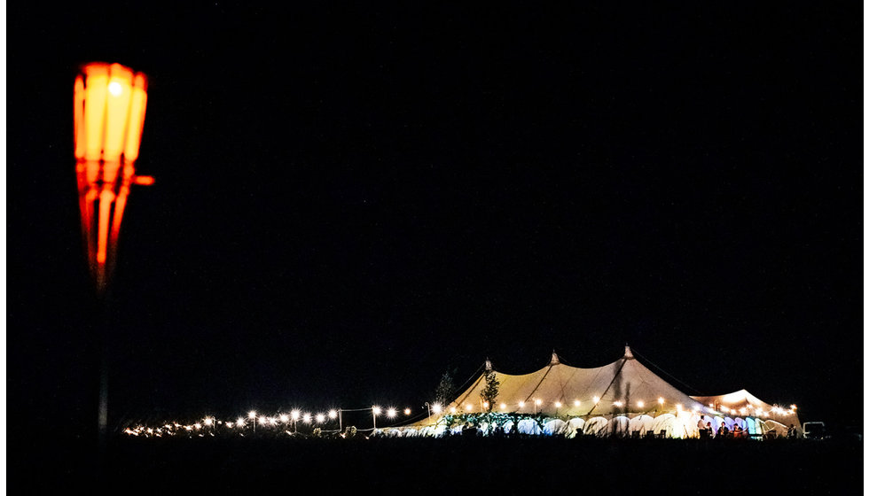 The marquee in the distance at night lit up by festoon lights and the light from within.
