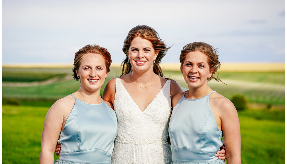 The bride and her bridesmaids. The bridesmaids wear sleeveless blue dresses.