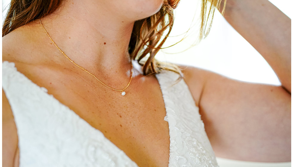 The bride wearing a delicate necklace and a sleeveless wedding dress.