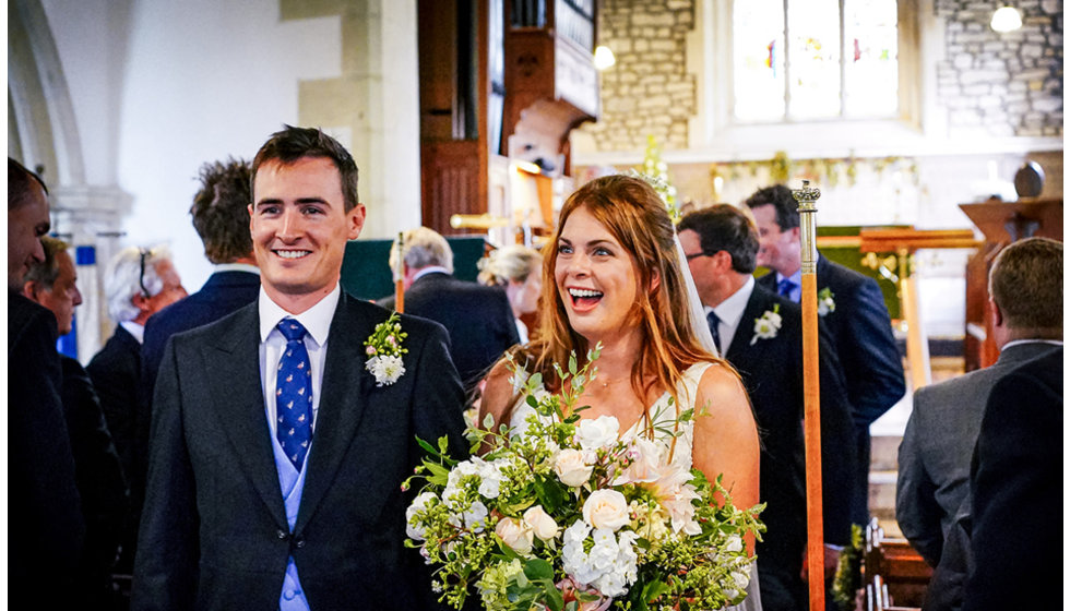 Victoria and Josh in the church. Victoria is holding a large beautiful wild bouquet of flowers.