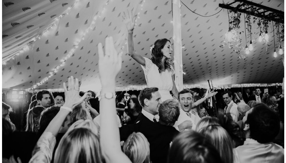 The bride on the some of the wedding guests shoulders at their marquee wedding.