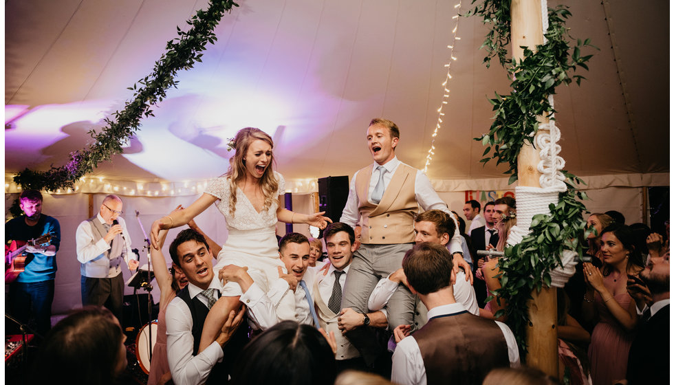 The bride and groom on the shoulders of their wedding guests in the marquee.