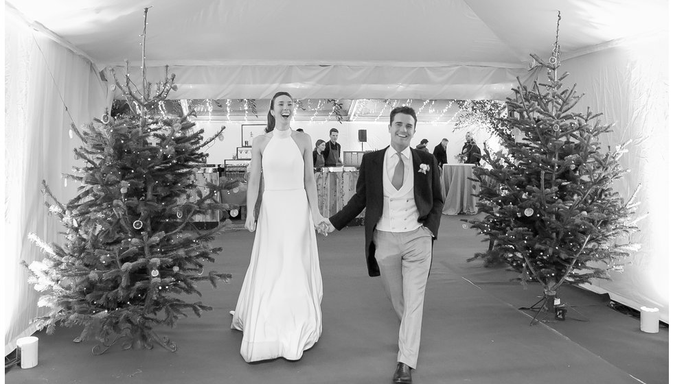 A bride and groom walking past Christmas trees in their tent.