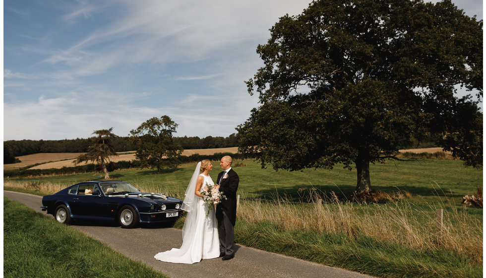 The bride and groom stand in front of one of their parents vintage cars.