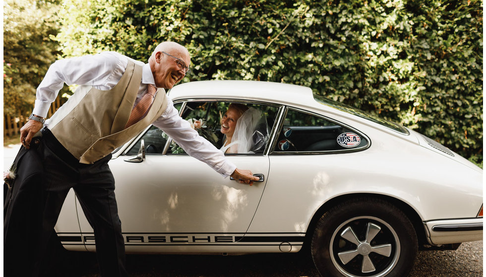The father of the bride opening the door of a vintage car for his daughter to get out.
