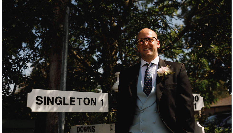 The groom standing next to a road sign saying 'singleton'.