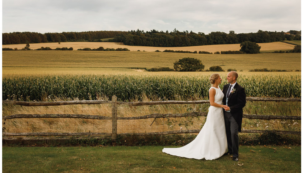 The bride and groom pose for a photo in front of rolling countryside in the background.