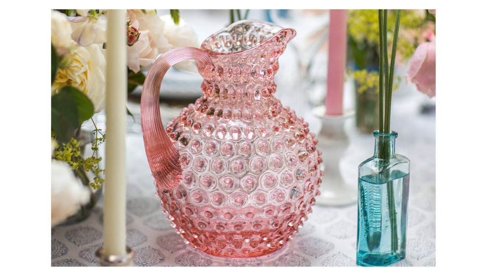 Pink hobnail jug on a table laid with flowers and candles.