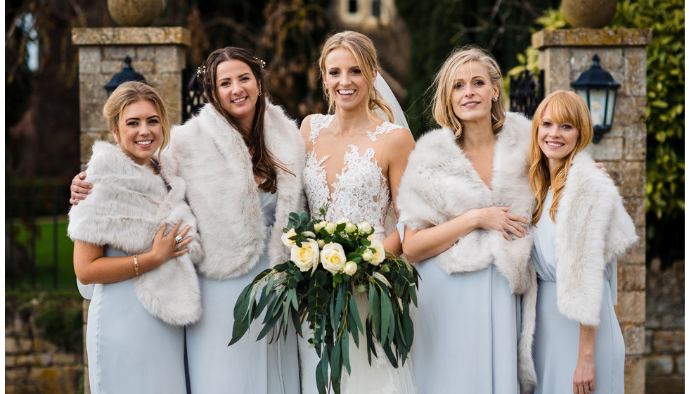The bridesmaids outside with the bride wearing faux fur shalls.
