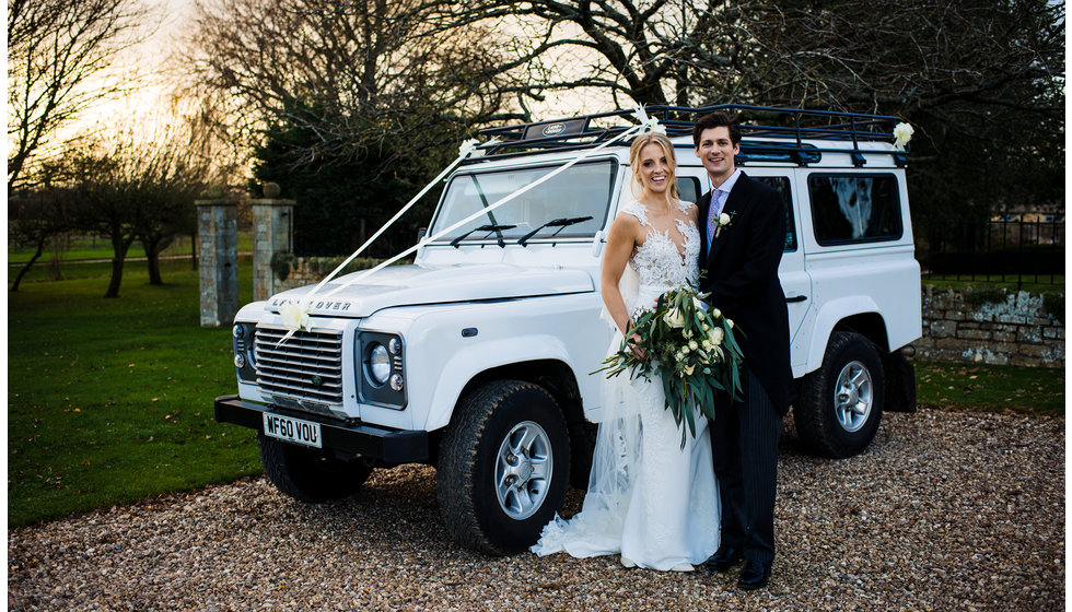 The couple pose in front of a white land rover discovery.