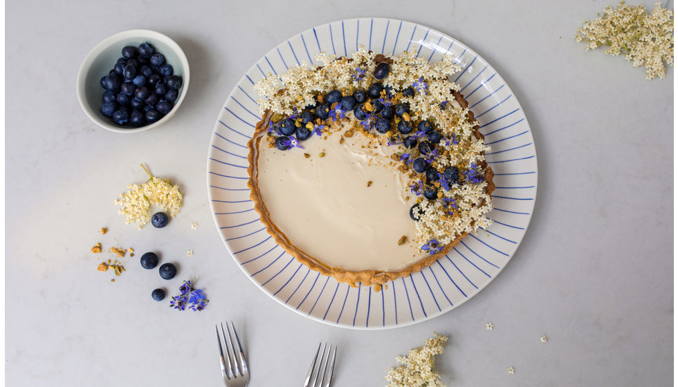 A beautifully presented blueberry tart on a large Nkuku round plate with blue tear detail.